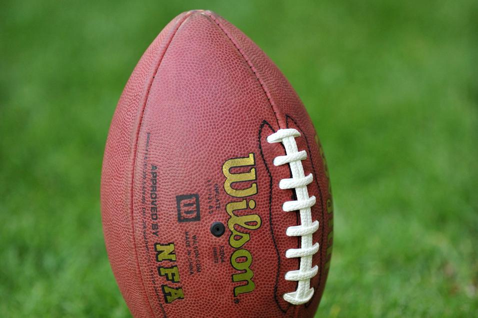 Ein American Football steht in einem Halter auf grünem Gras.