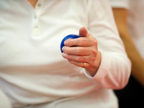 Nahaufnahme einer Hand, die einen blauen Ball hält, während die Person in einem weißen Oberteil sitzt.