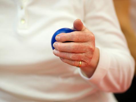 Nahaufnahme einer Hand, die einen blauen Ball hält, während die Person in einem weißen Oberteil sitzt.