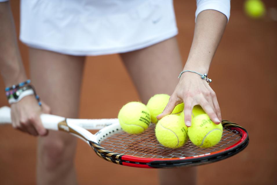 Hand greift mehrere gelbe Tennisbälle auf einem Tennisschläger, während die andere Hand die Schlägerhaltung stabilisiert.