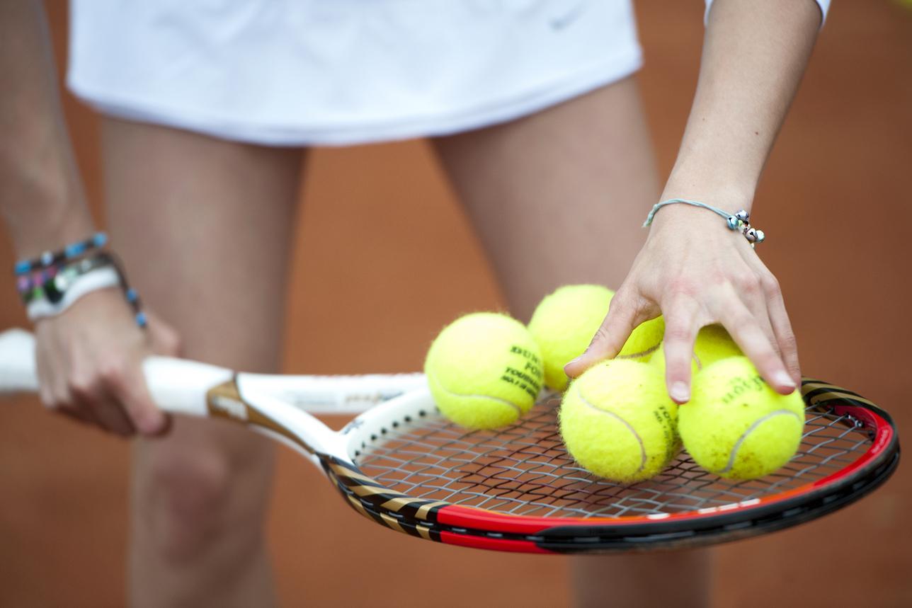 Hand greift mehrere gelbe Tennisbälle auf einem Tennisschläger, während die andere Hand die Schlägerhaltung stabilisiert.